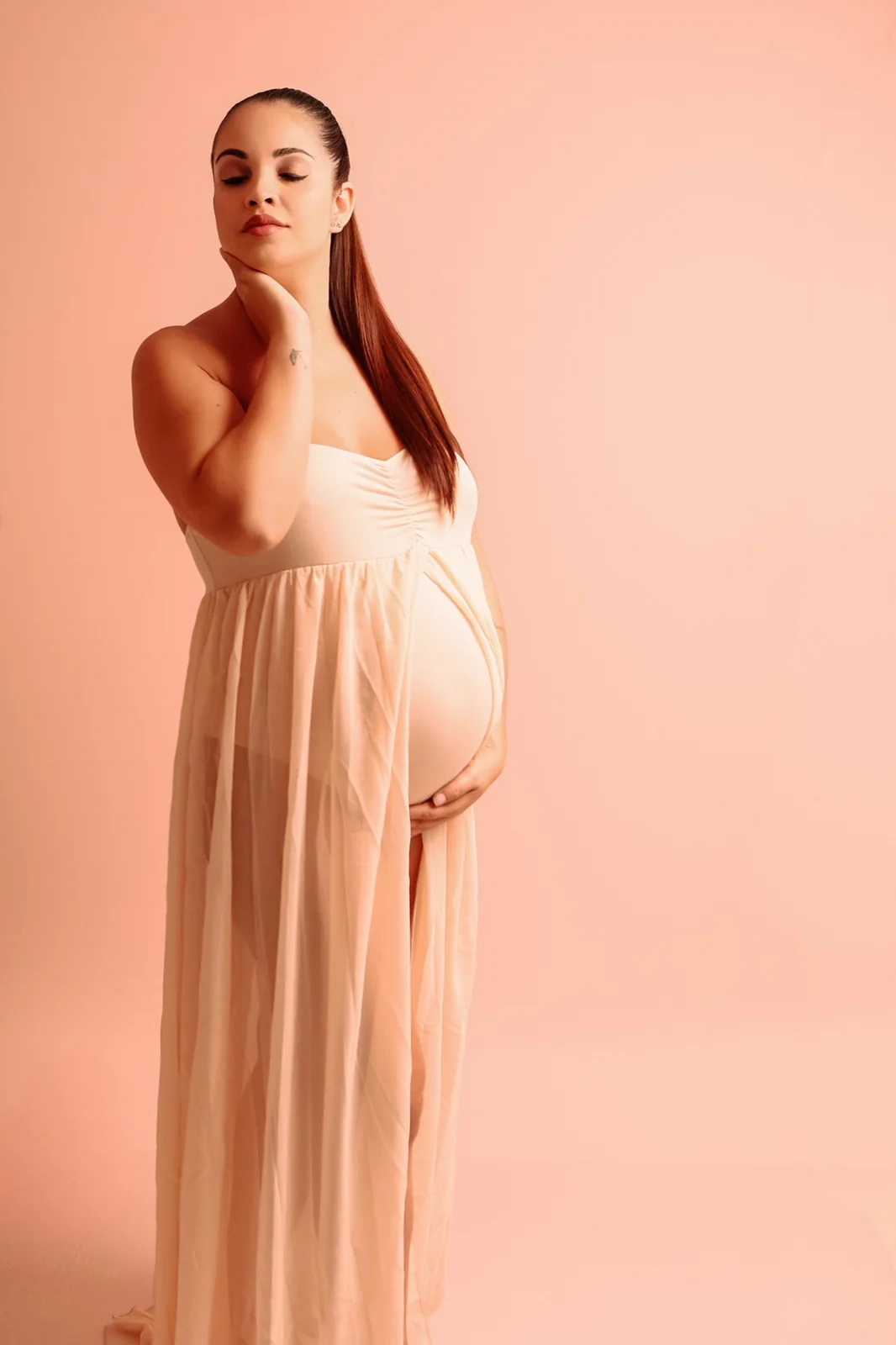Gestante em vestido claro em estúdio com fundo pêssego